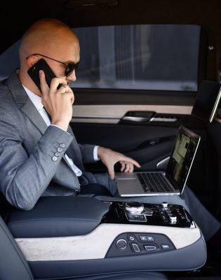 handsome businessman using his mobile phone in a modern car with a driver in center of the city. Concept of business, success, traveling, luxury.